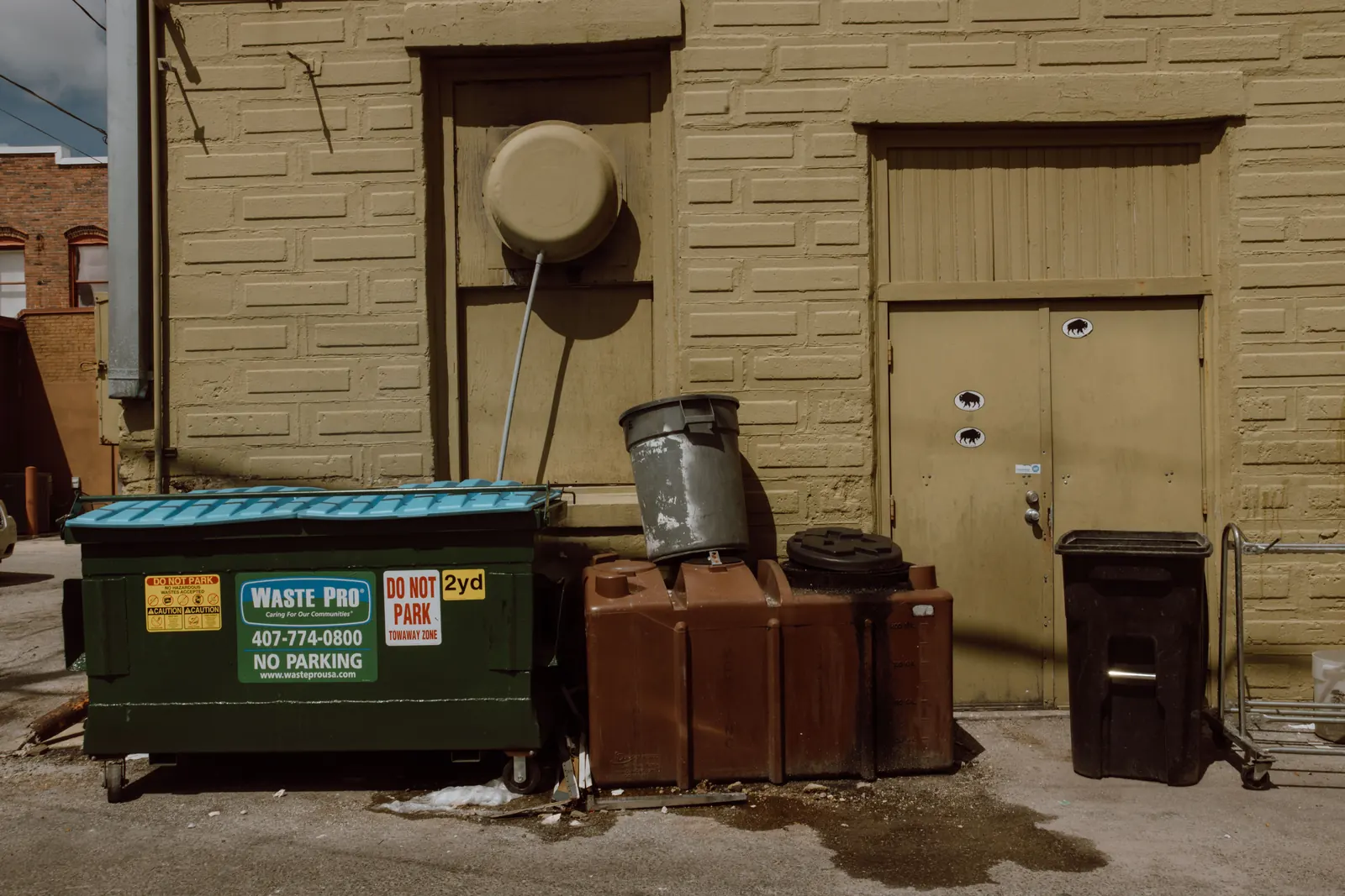 A front-load dumpster and drums beside a service door