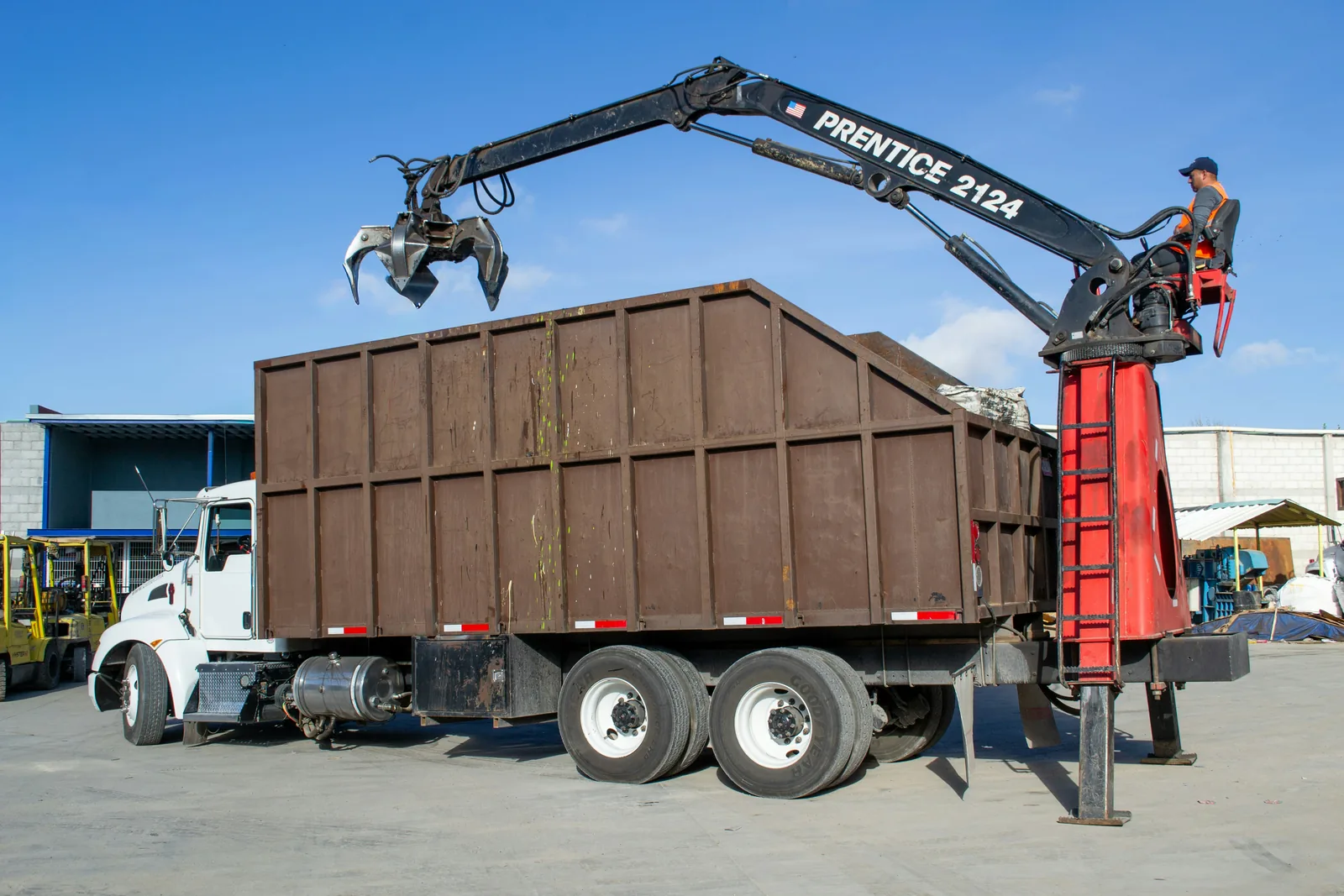 A grapple truck loading a high-sided scrap container