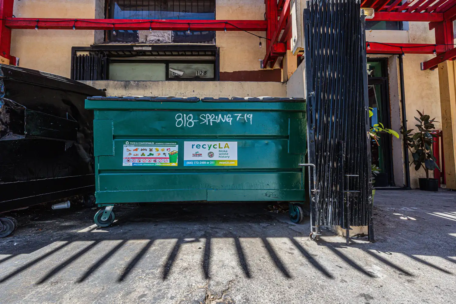 A green front-load dumpster behind an alley gate