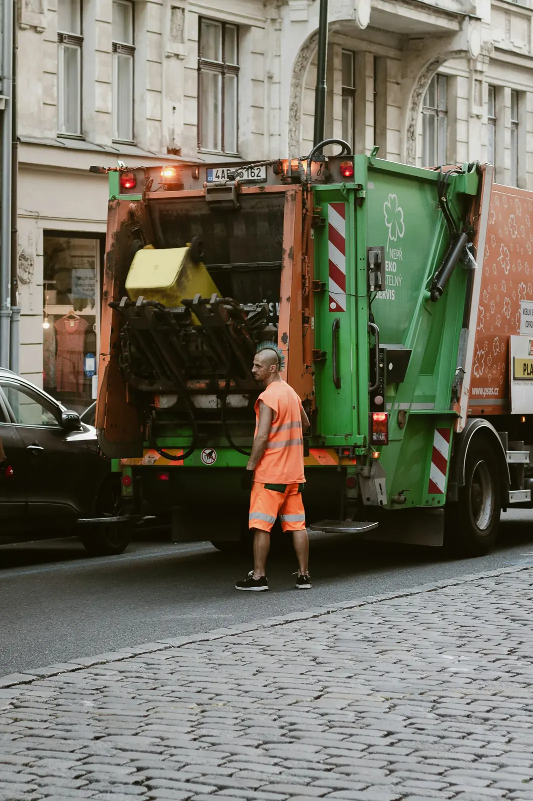 A rear-load refuse truck working a cobbled street