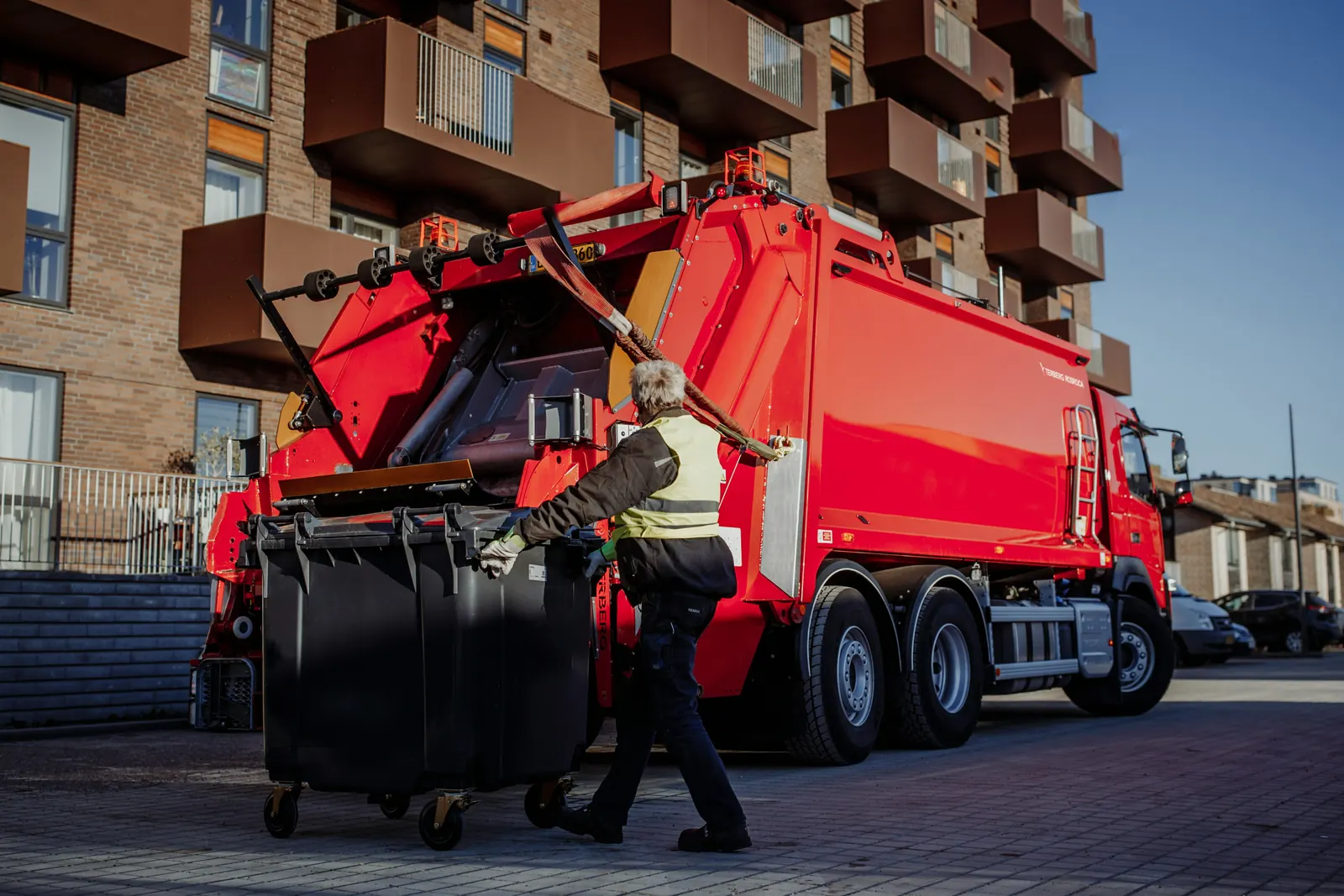 A red refuse truck taking a four-wheel container