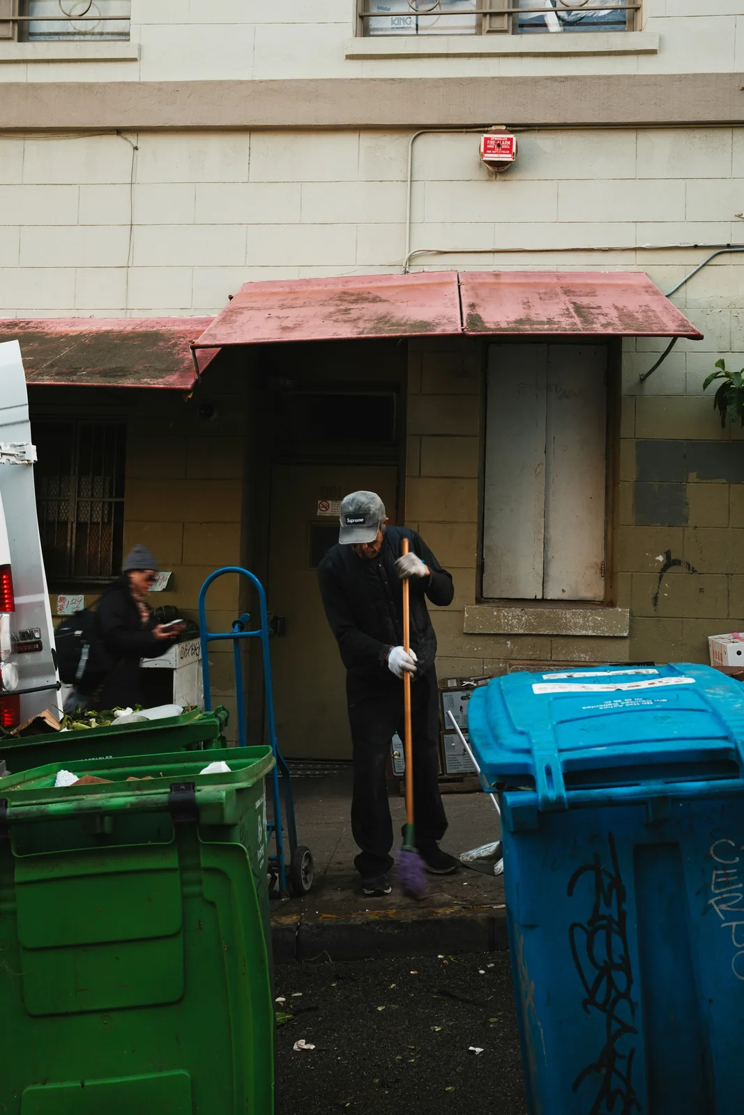 Sweeping up behind green and blue bins